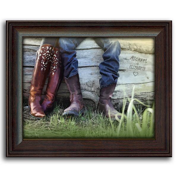 This western style art is a closeup of two people wearing cowboy boots resting on a fallen tree -framed under glass
